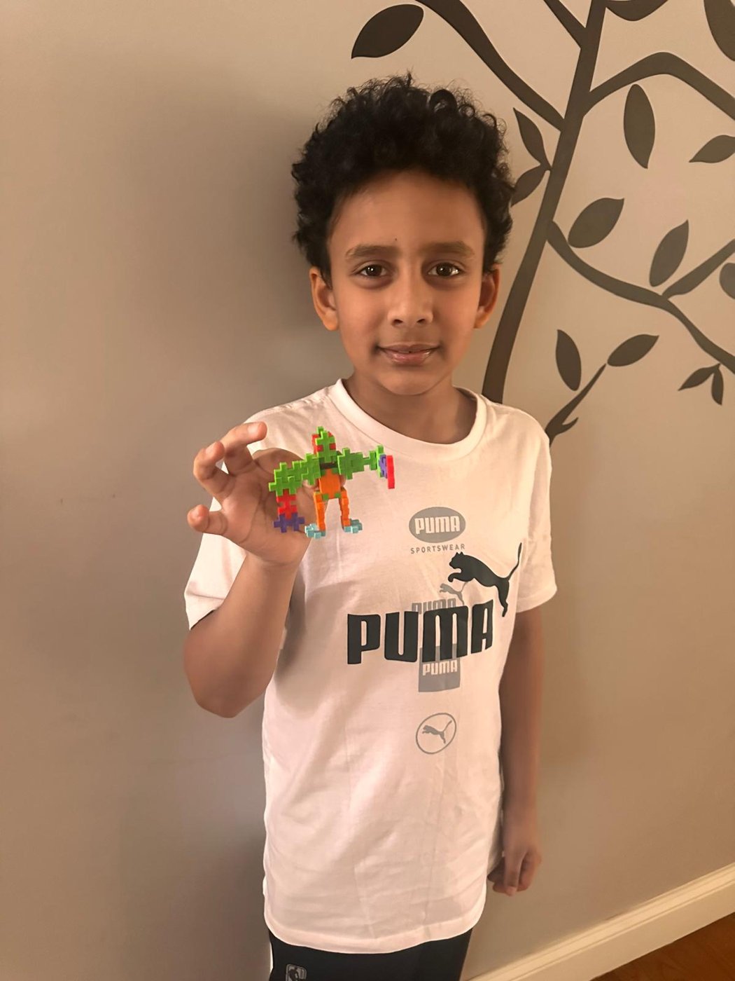 A child holding up a small figure made of green and orange building blocks