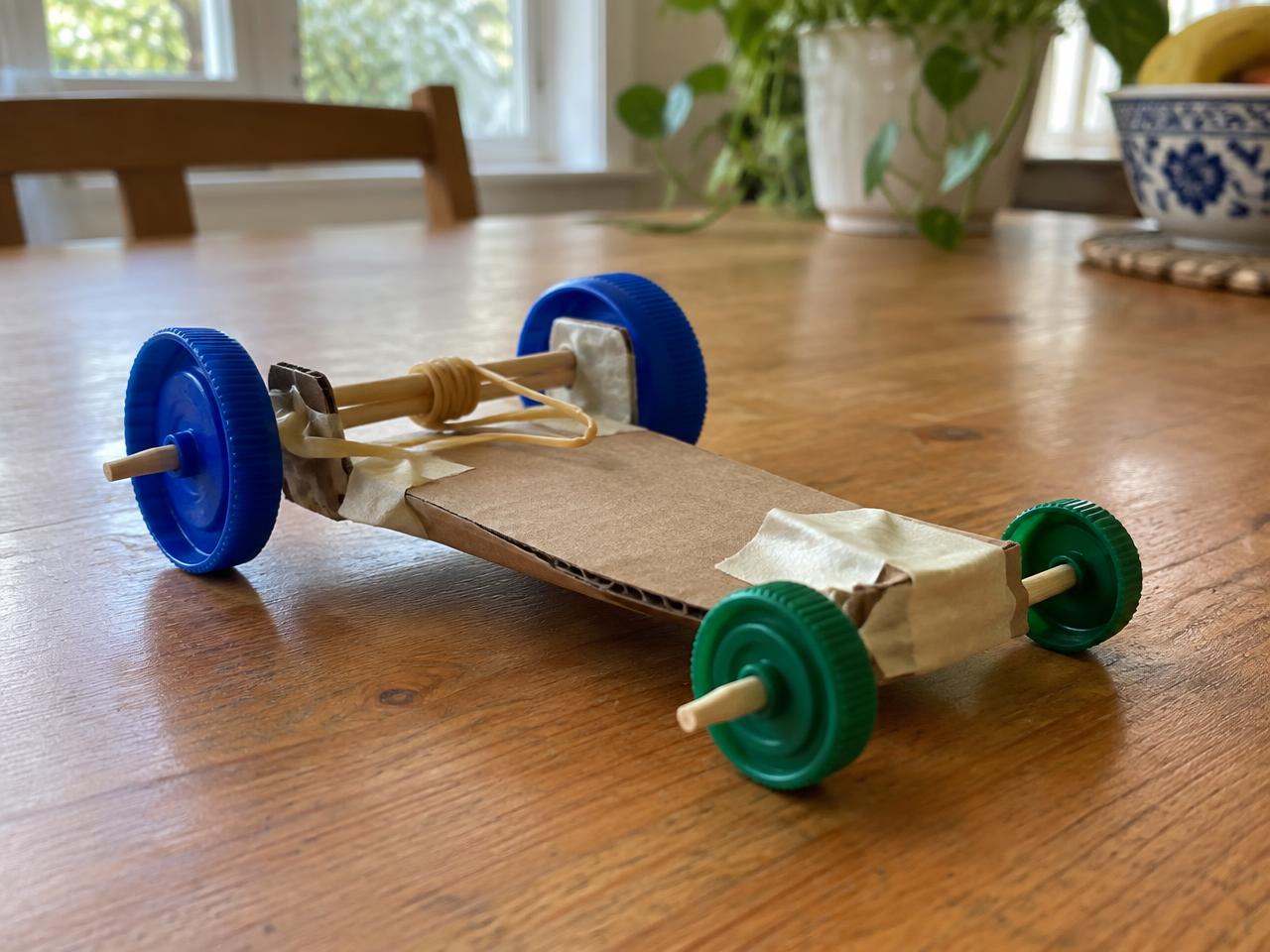 Homemade rubber band car with bottle-cap wheels on a kitchen table